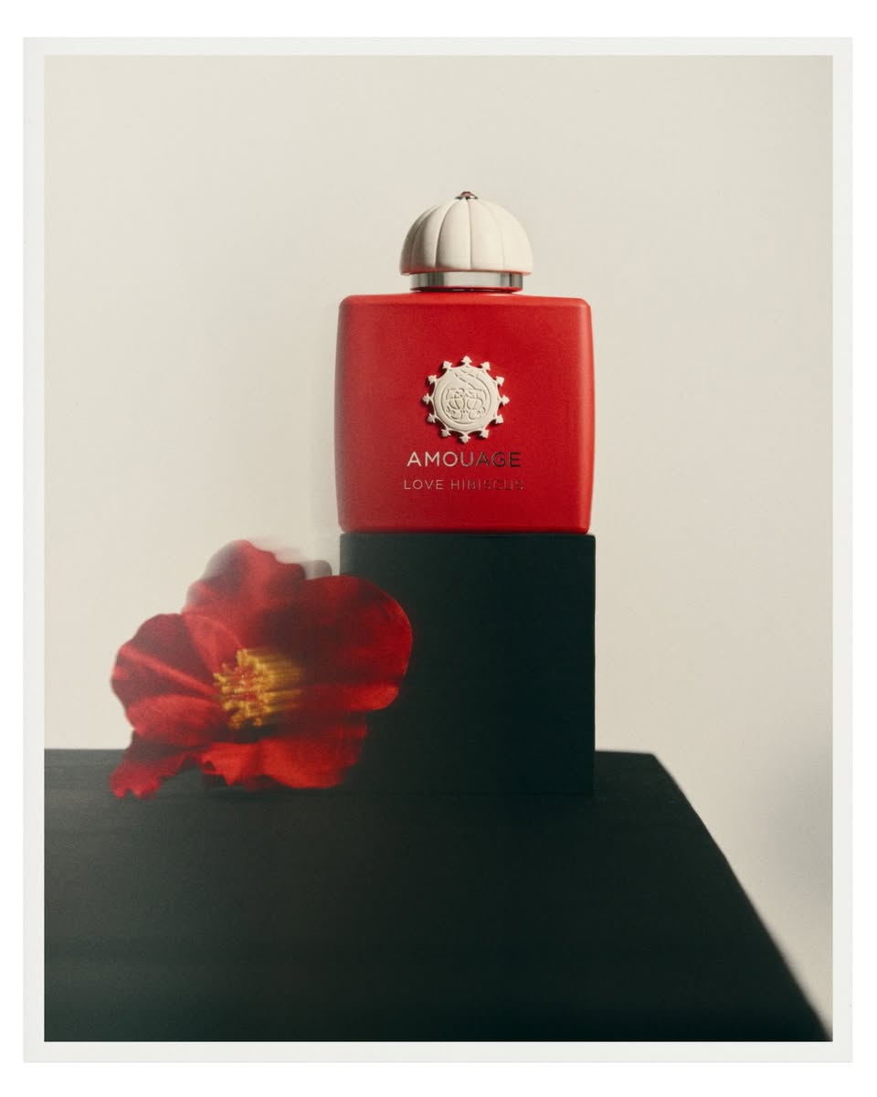 Amouage Love Hibiscus red bottle with white cap beside a floral element