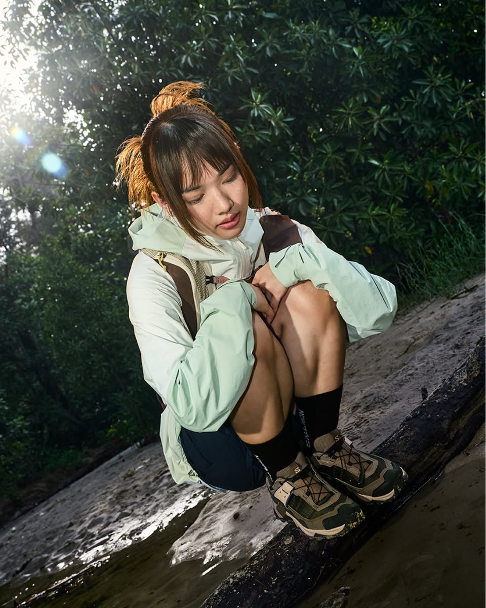Person wearing light green hooded jacket crouching on log in forest