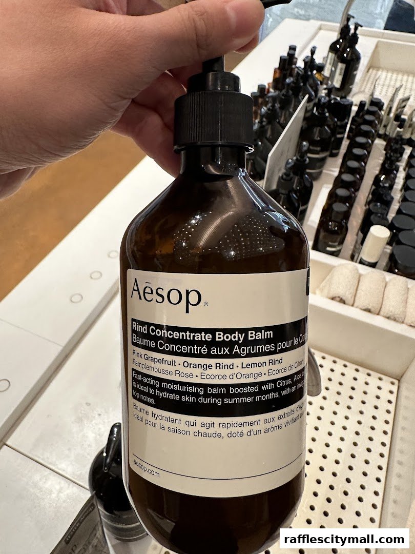 A hand holds an Aesop Rind Concentrate Body Balm bottle with product details visible.