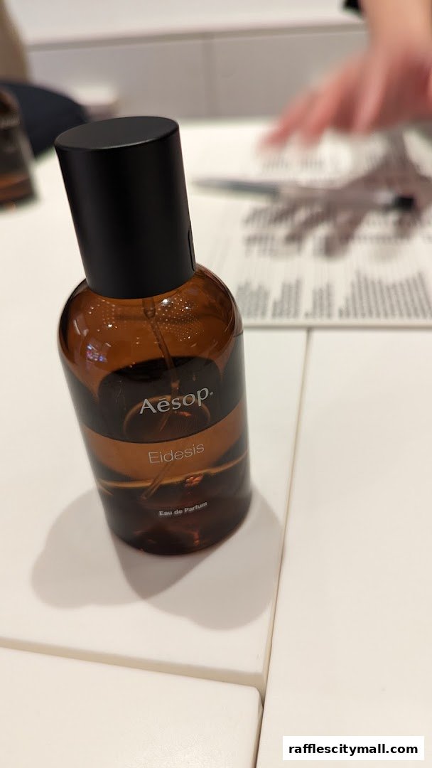 An Aesop Eidesis Eau de Parfum bottle sits on a white surface with a blurred background.