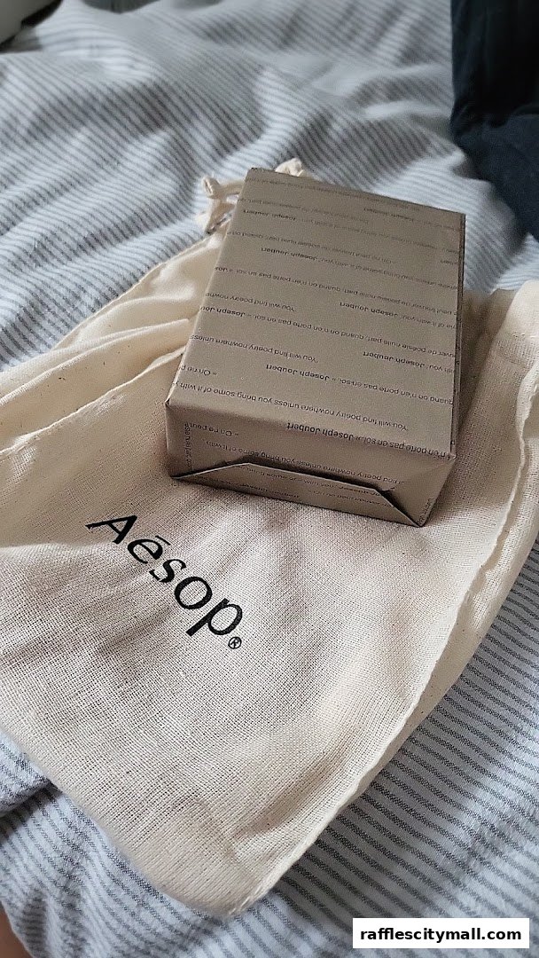 An Aesop branded gift bag with a small, wrapped product inside, resting on a striped surface.