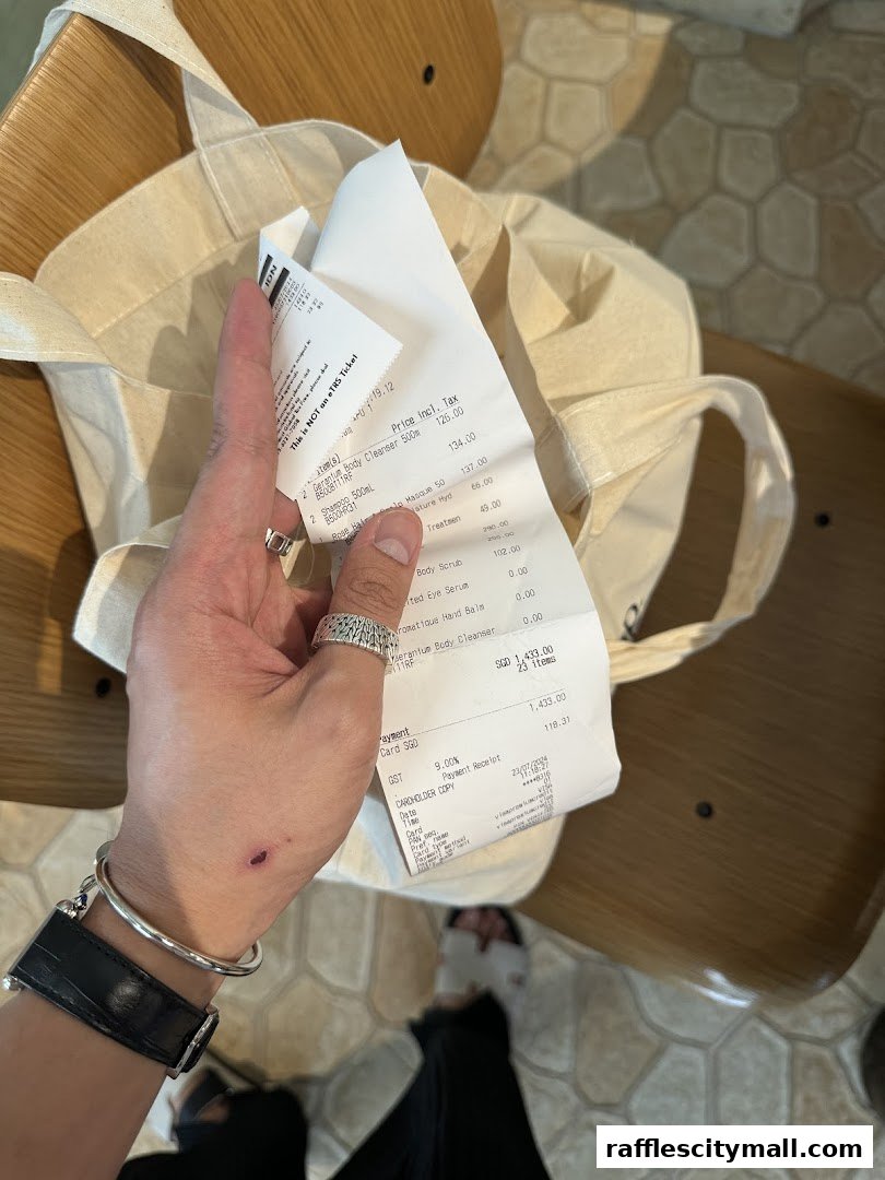 A hand holds a receipt from Aesop, with a canvas tote bag in the background.