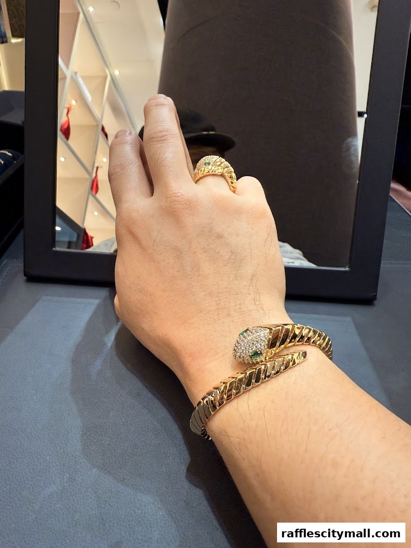A person tries on a gold snake-shaped bracelet and ring with green and white stones.