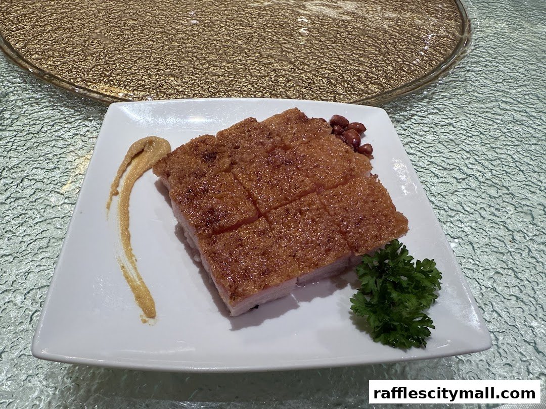 A plate of crispy roasted pork with a side of mustard sauce, peanuts, and parsley.