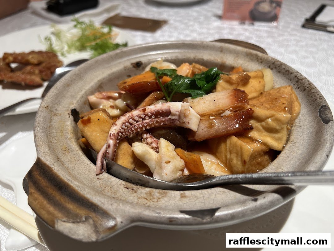 A close-up of a clay pot dish with squid, tofu, and meat in a savory sauce.
