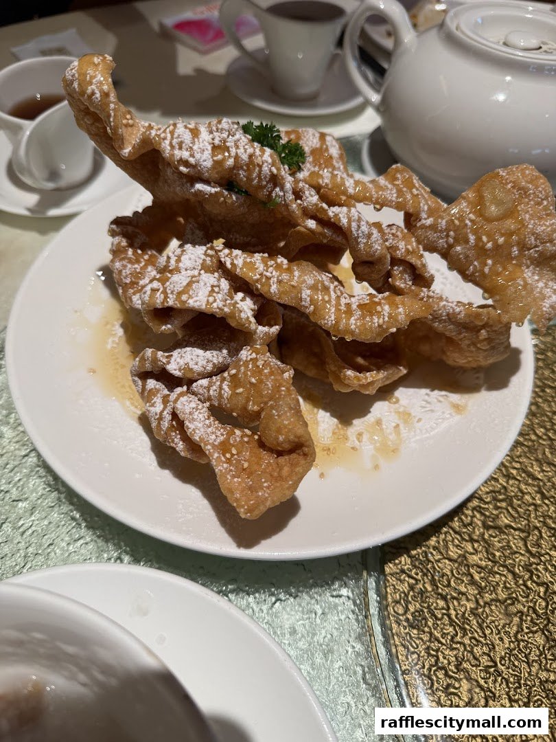 A plate of crispy fried dough drizzled with syrup and dusted with powdered sugar.