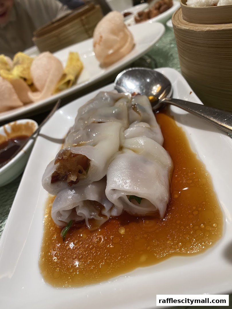 A close-up of delicious steamed rice noodle rolls with savory sauce, served at Asia Grand Restaurant.