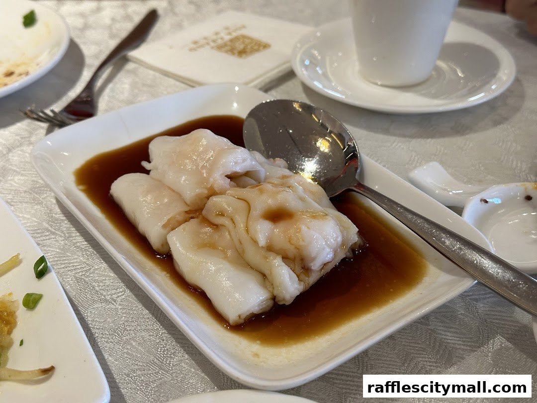A close-up of steamed rice noodle rolls with shrimp, served in a savory sauce.