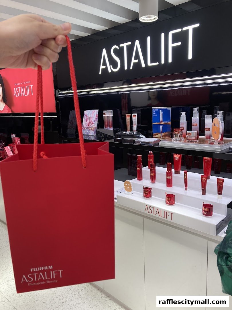 A hand holds a red shopping bag in front of the Astalift store display.