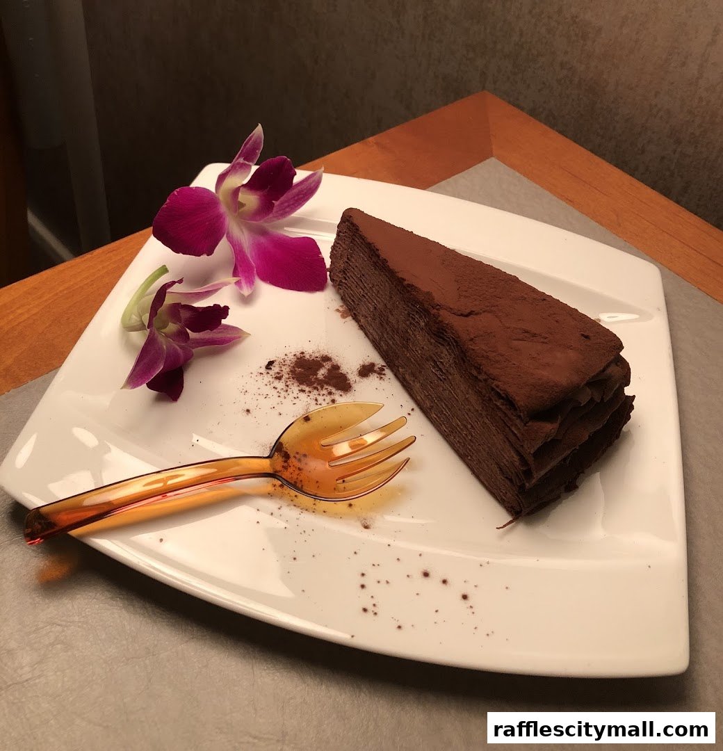 A slice of rich chocolate cake with cocoa powder and a decorative orchid.