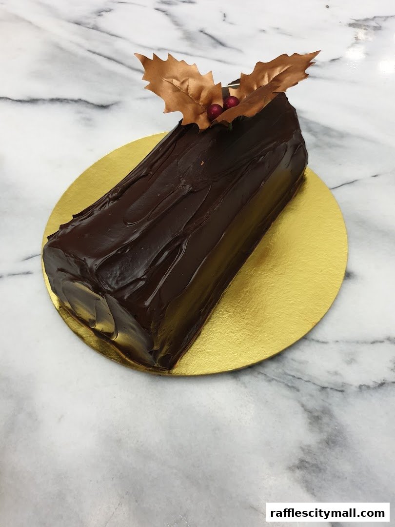 A chocolate log cake decorated with gold leaves and berries on a gold platter.