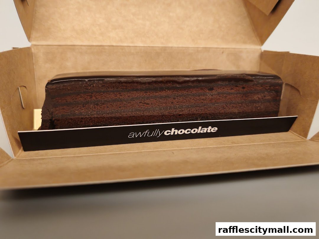 A slice of rich chocolate cake with multiple layers in a cardboard box.