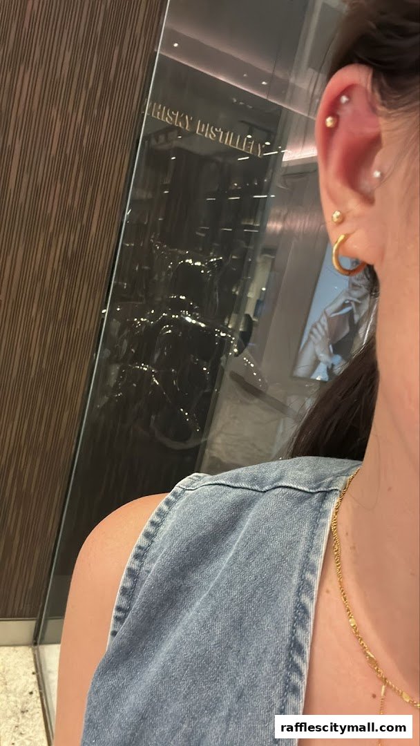 A person's ear with multiple piercings, reflecting a store with "WHISKY DISTILLERY" signage.