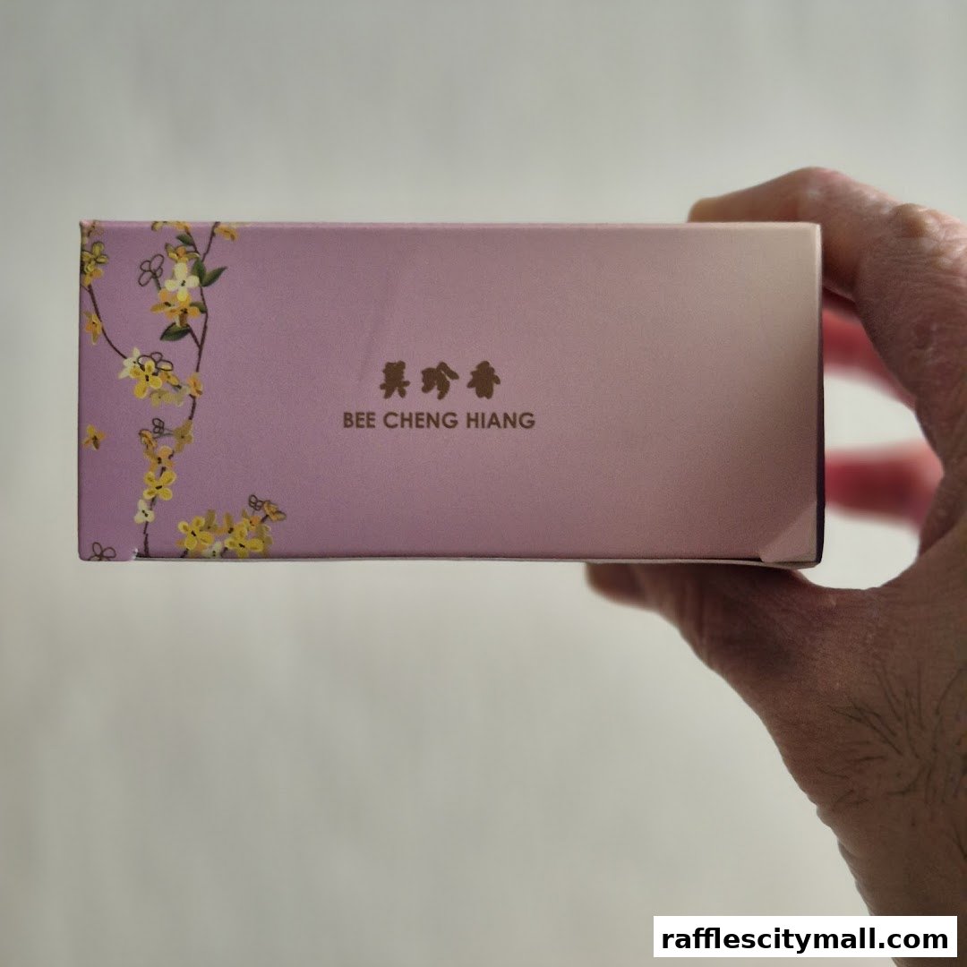 A hand holds a pink box with floral designs and the Bee Cheng Hiang logo.
