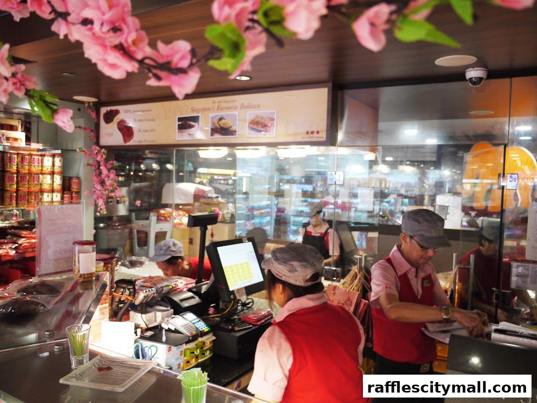 Staff members working behind the counter at a Bee Cheng Hiang store, decorated with pink flowers.