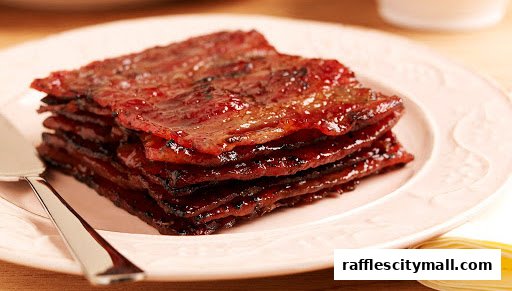 A stack of glistening, sweet pork jerky slices on a pink plate with a serving utensil.