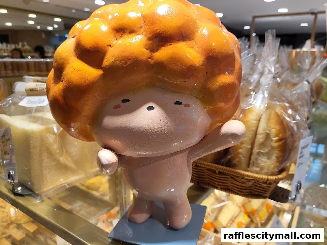 A cute cartoon figurine stands in front of a display of freshly baked bread and pastries.