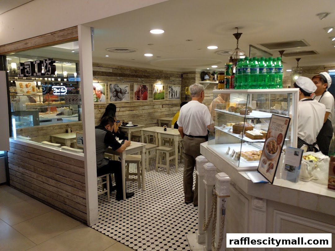 Interior of a BreadTalk bakery with customers and staff, showcasing baked goods and seating.