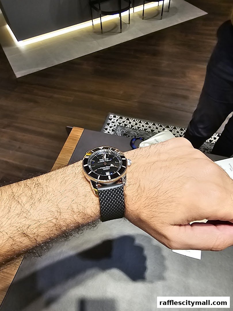 A close-up of a person's wrist wearing a Breitling watch with a black mesh strap.