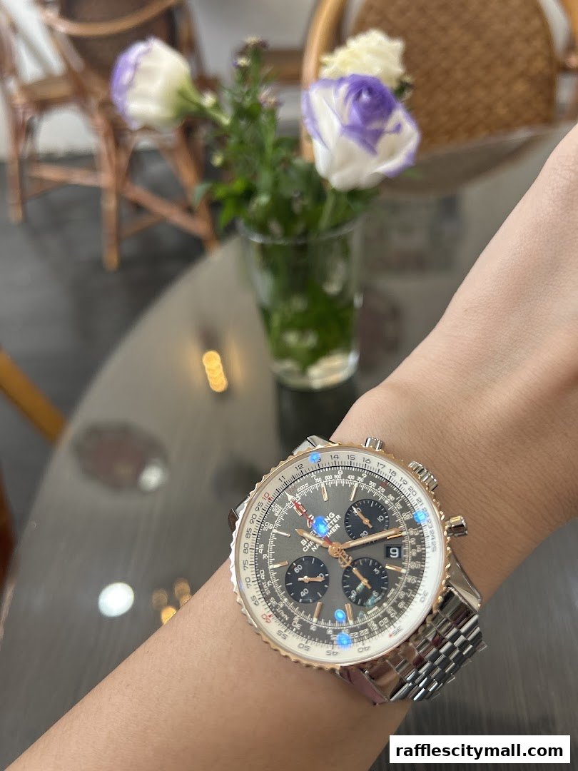 A close-up of a Breitling watch on a wrist, with flowers in the background.