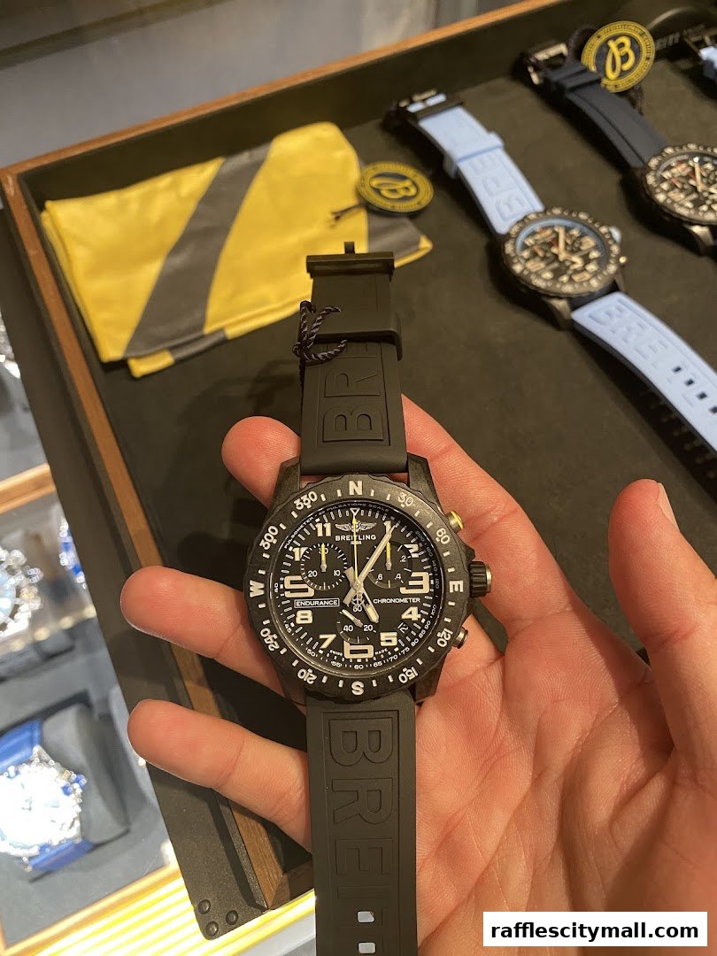 A hand holds a Breitling Endurance Pro watch with a black strap.