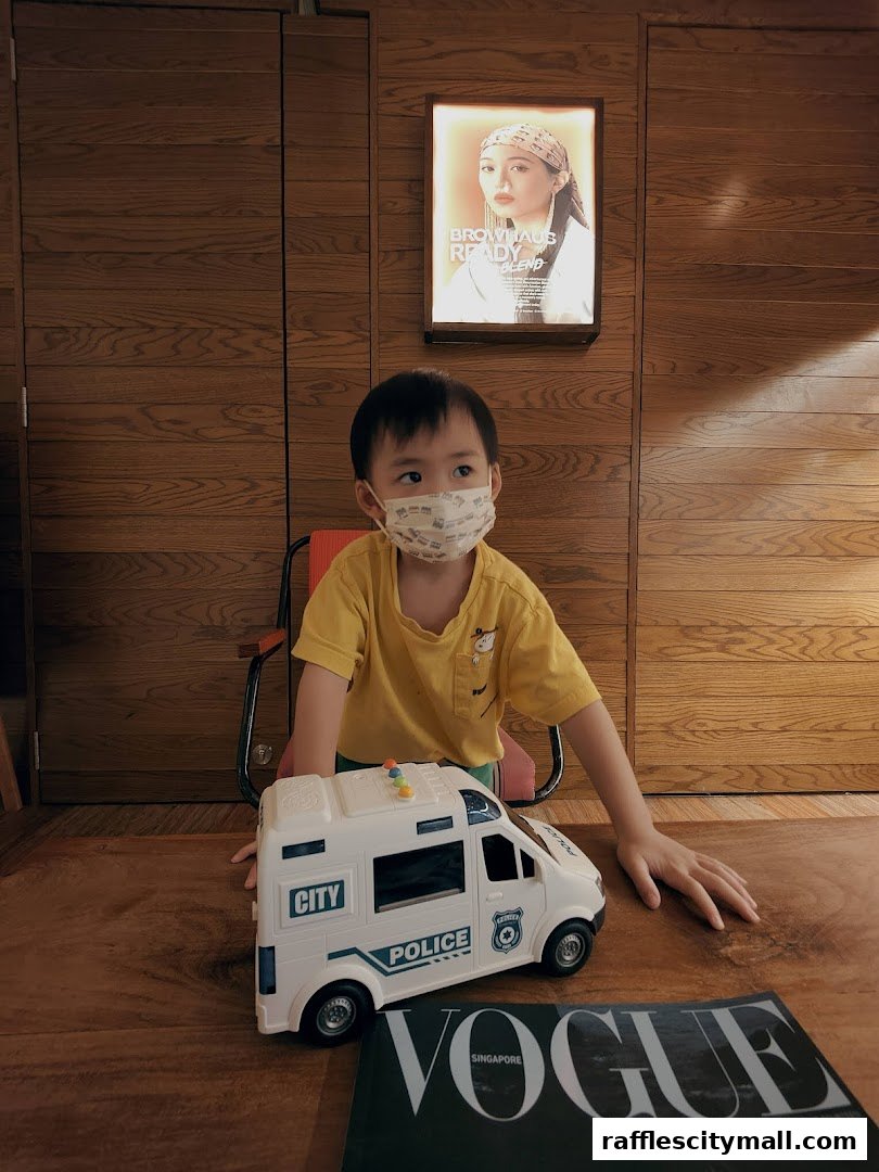 A young boy wearing a mask sits with a toy police car and a Vogue magazine.