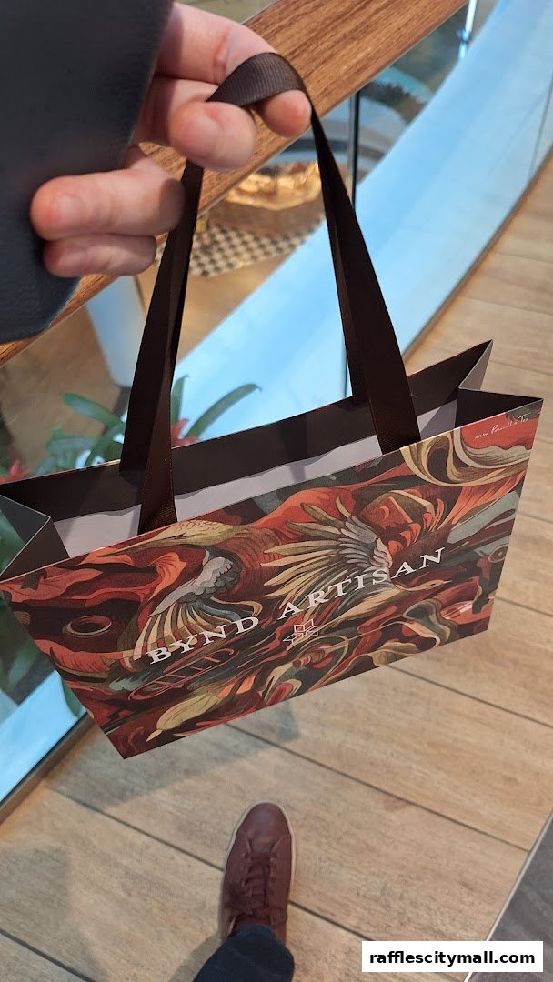 A hand holds a shopping bag with intricate artwork and the shop name 'BYND ARTISAN'.