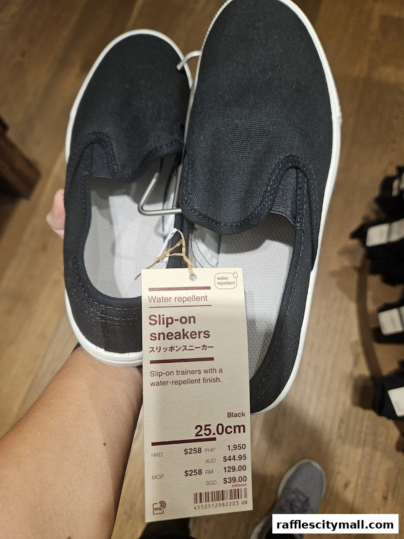 A person holds a pair of black slip-on sneakers with a price tag.