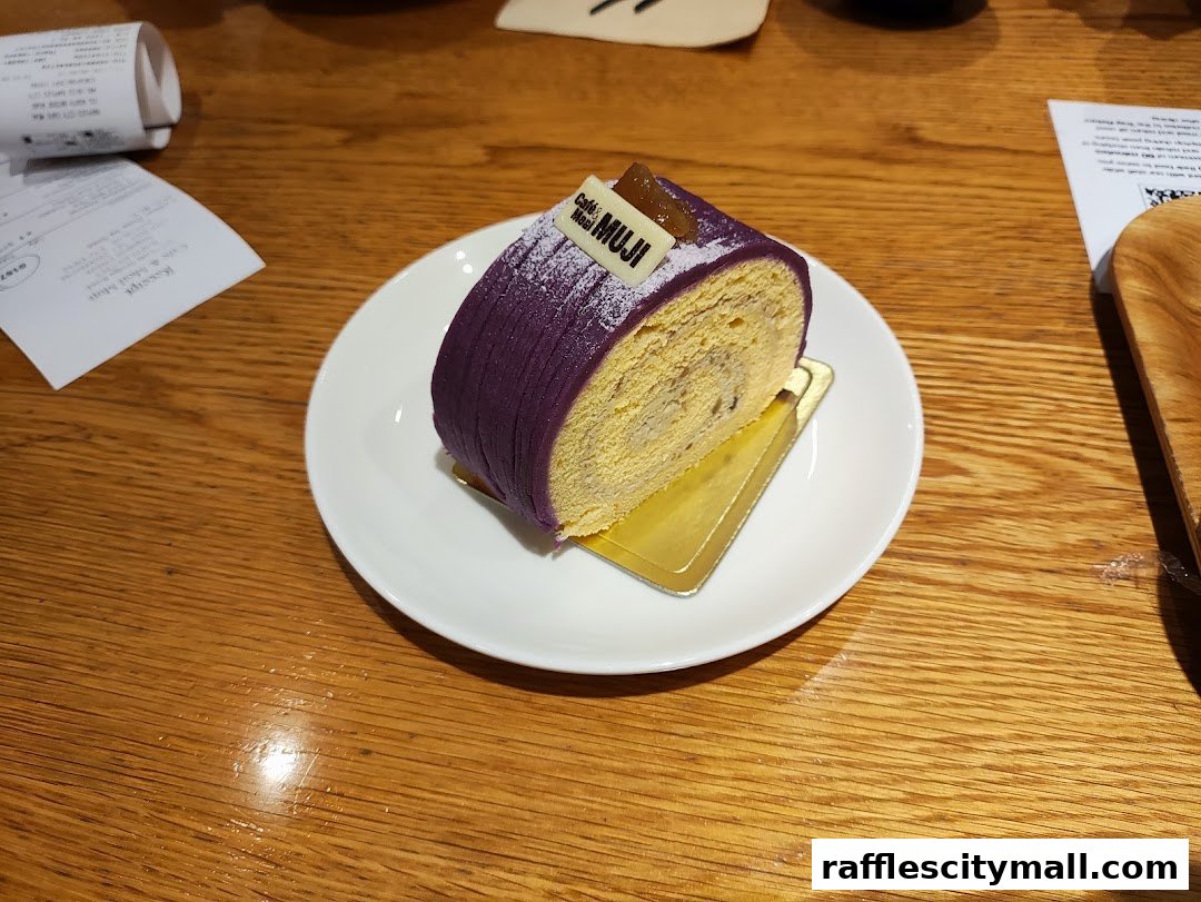 A slice of purple yam roll cake with MUJI branding on a white plate.