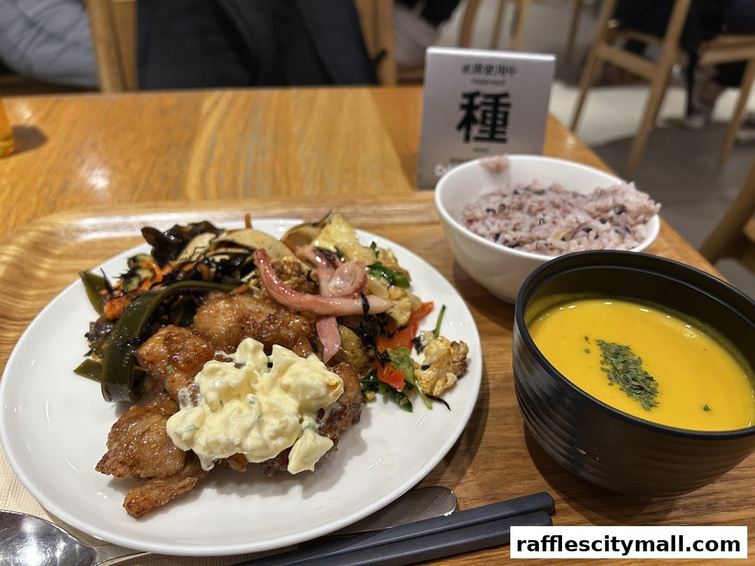 A plate of food with fried chicken, vegetables, rice, and soup on a wooden table.