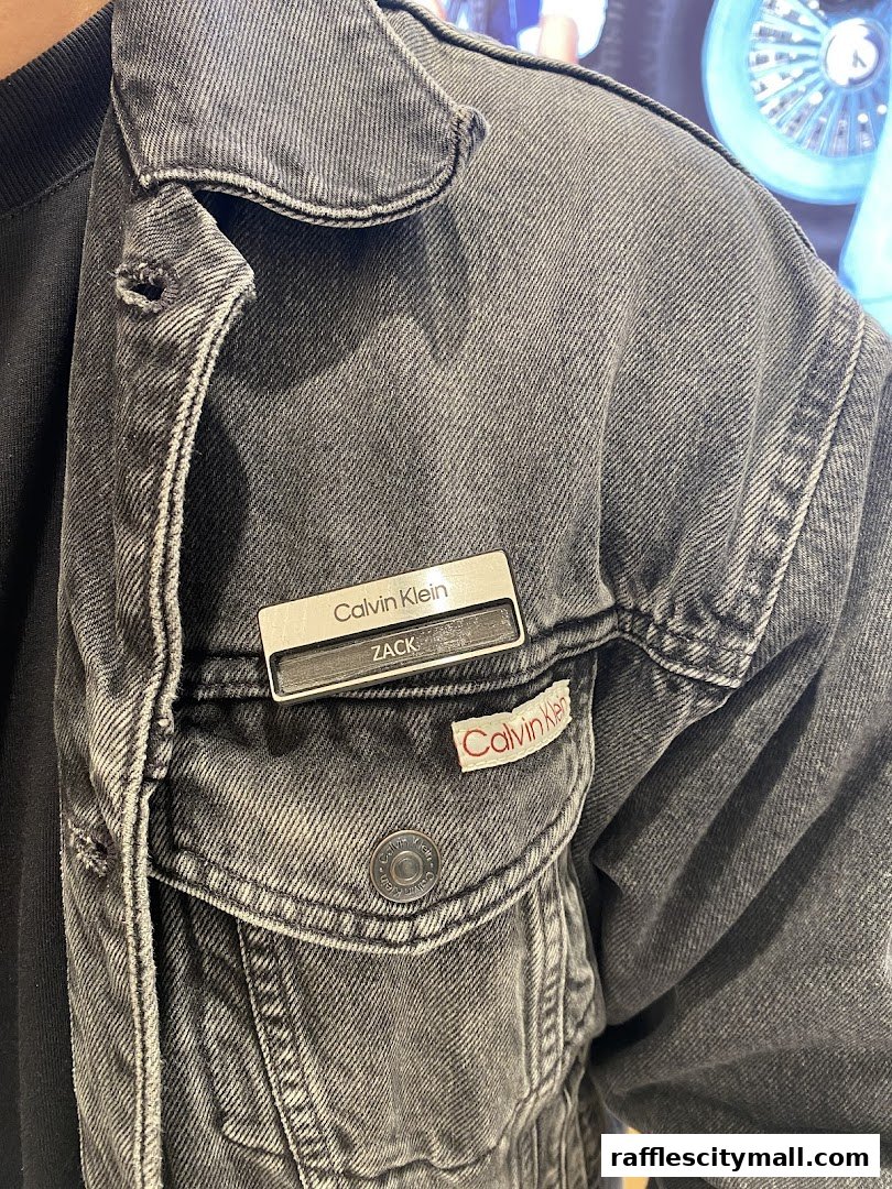 Close-up of a person wearing a grey denim jacket with Calvin Klein branding.