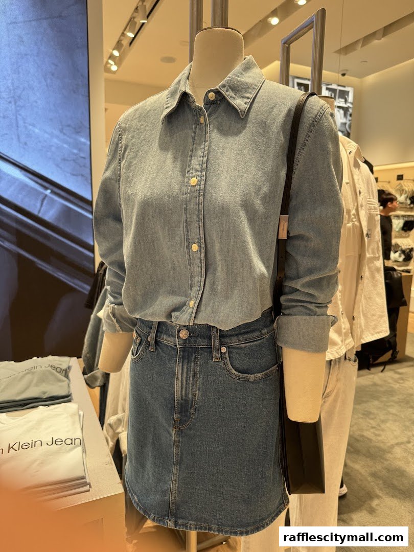 A mannequin displays a denim shirt and skirt outfit with a black bag at Calvin Klein.