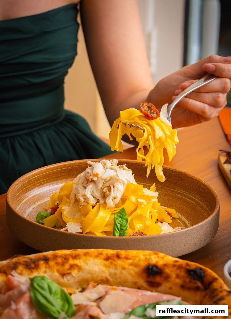 A person enjoys a plate of pasta with crab meat and a pizza in the foreground.