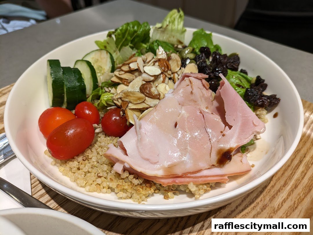 A close-up of a healthy salad with ham, quinoa, vegetables, nuts, and dried fruits.