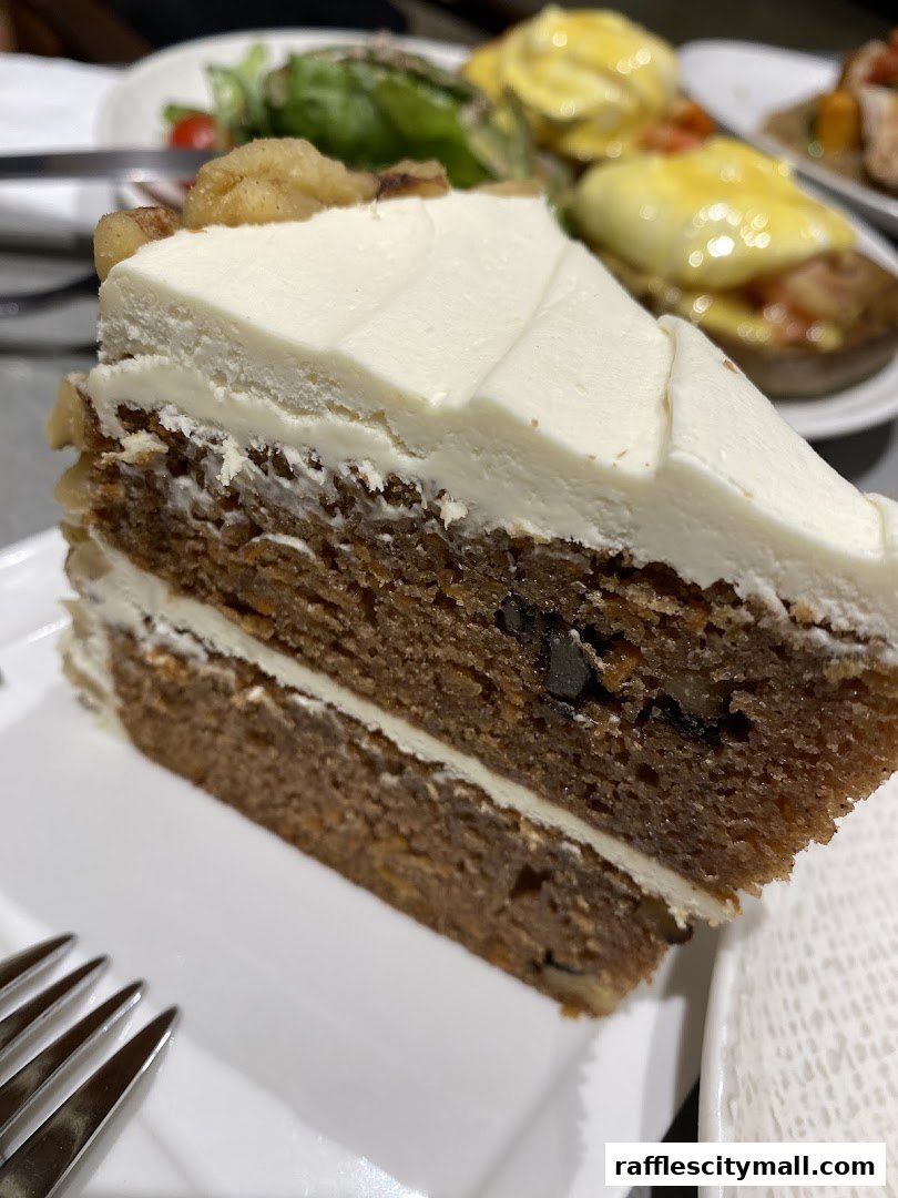 A slice of moist carrot cake with cream cheese frosting and walnuts, served on a white plate.