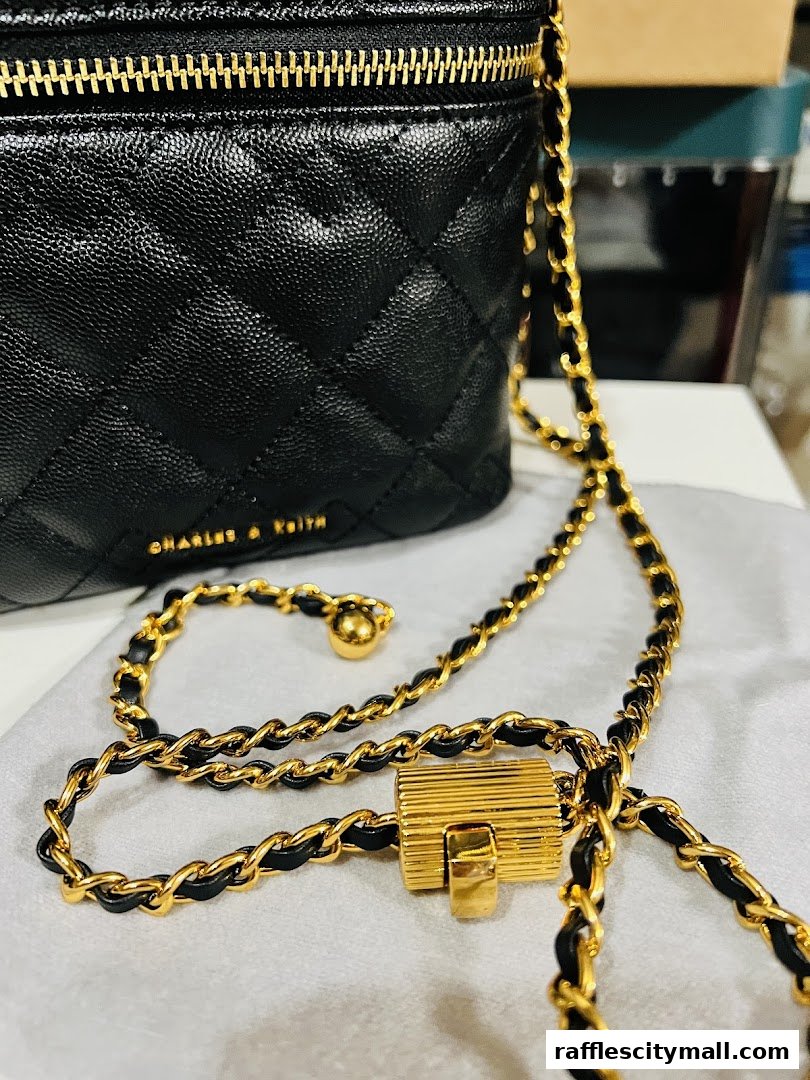 A close-up of a black quilted CHARLES & KEITH handbag with a gold chain strap.
