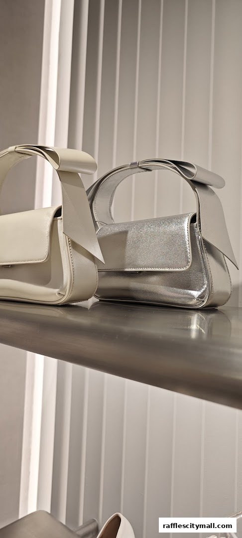 Two stylish handbags, one cream and one silver, displayed on a shelf.
