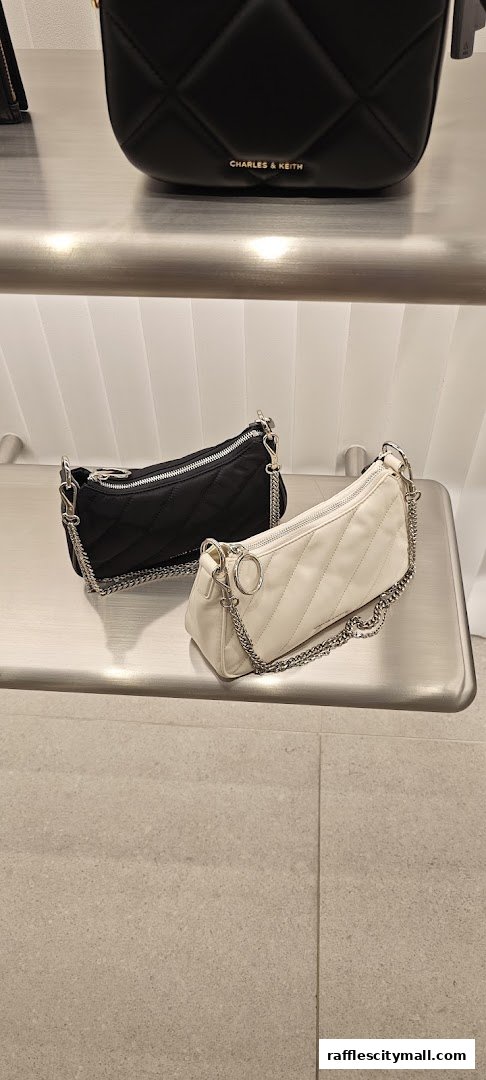 Two stylish quilted shoulder bags, one black and one cream, displayed on a shelf.