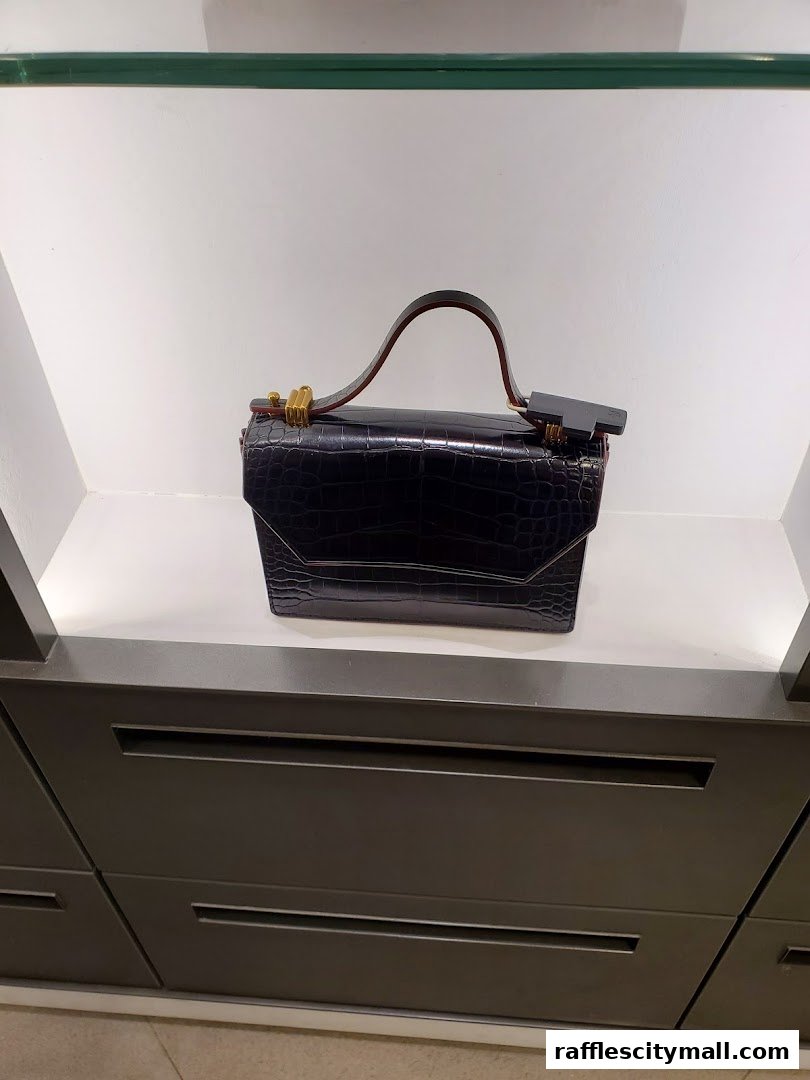 A black crocodile-textured handbag with a top handle is displayed on a white shelf.