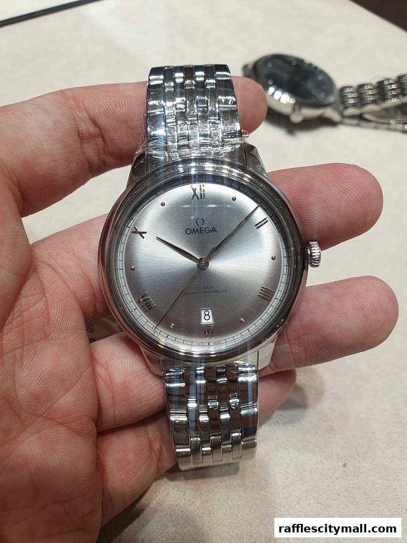 A hand holds a silver Omega watch with a grey dial and date window.