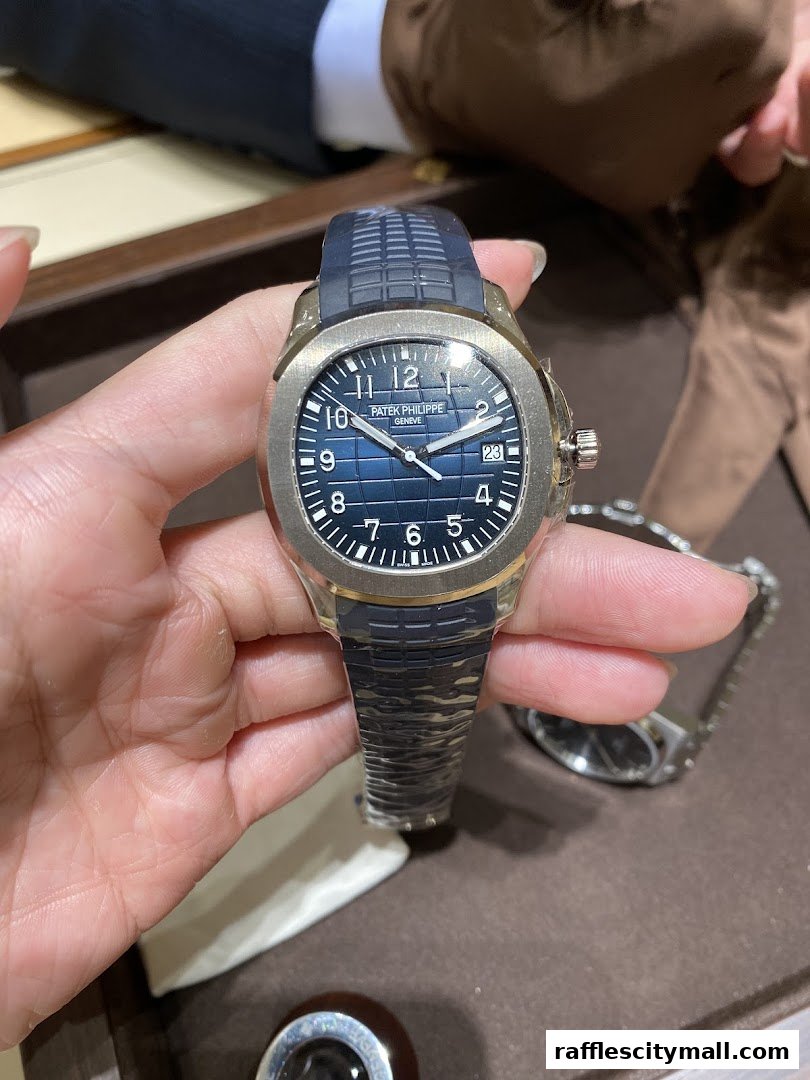 A hand holds a luxury Patek Philippe watch with a blue dial and rubber strap.
