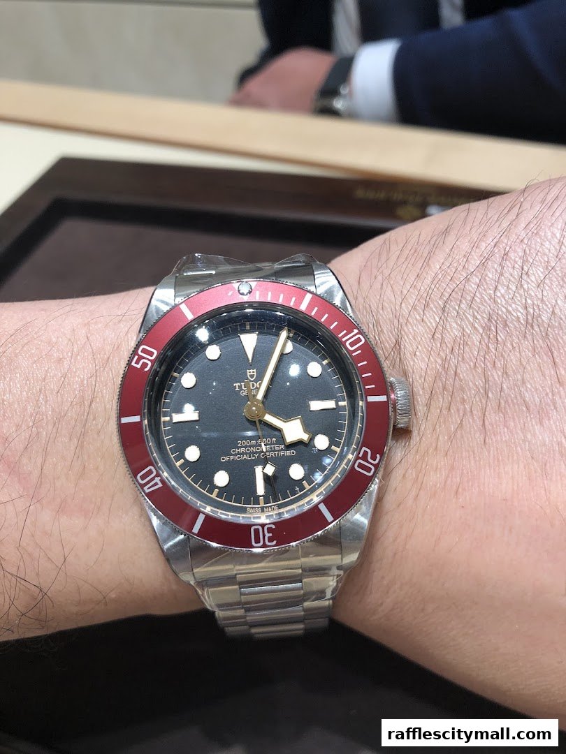 A close-up of a Tudor watch with a red bezel on a person's wrist.
