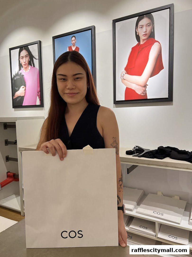 A person holds a COS shopping bag in front of fashion campaign images.