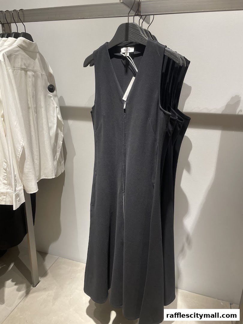A black sleeveless dress with a zipper hangs on a rack next to a white shirt.