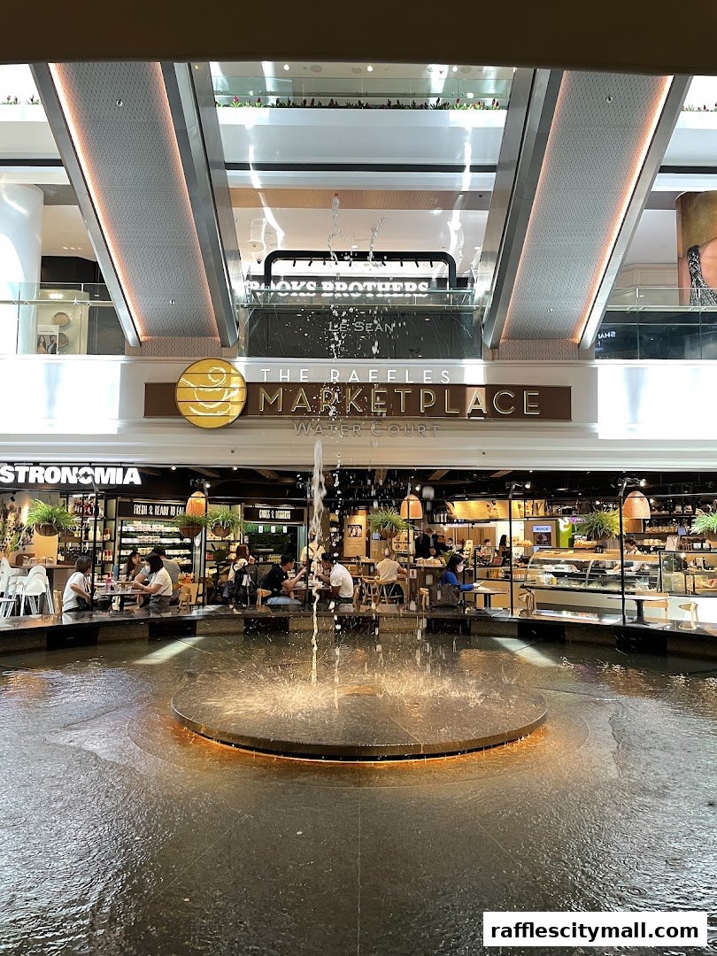 A fountain in front of a marketplace with seating areas and shops.