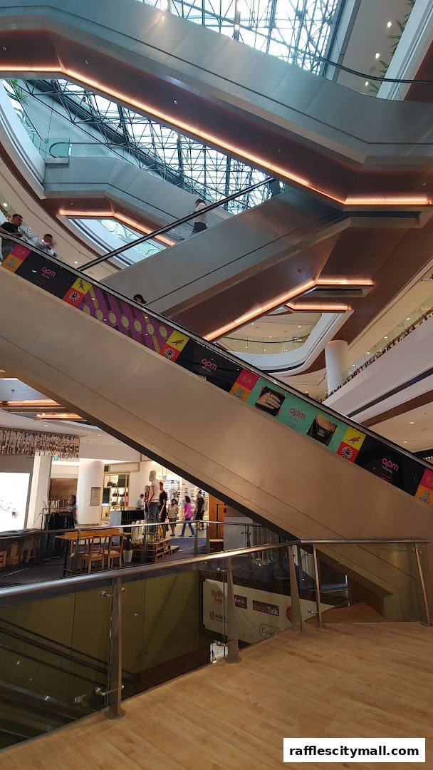 Interior view of a modern shopping mall with escalators and people.