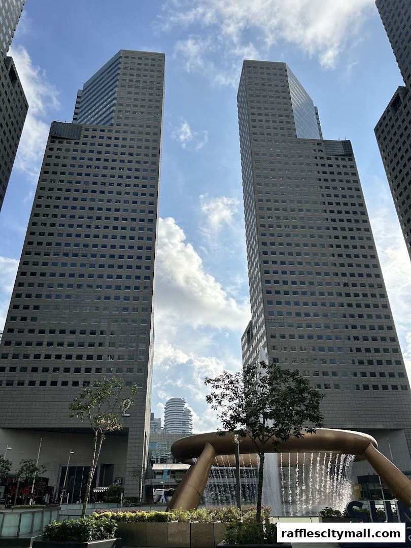 Tall modern skyscrapers and a large fountain in a city plaza under a cloudy sky.