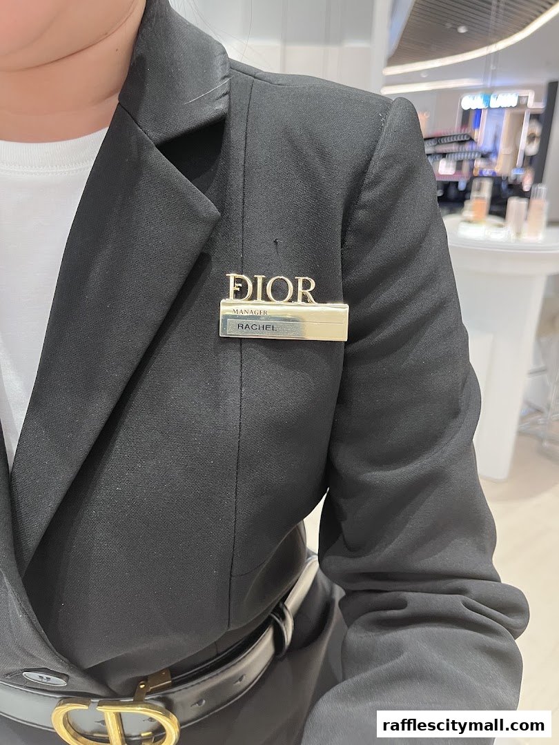 A person wearing a black blazer with a Dior name tag and belt.