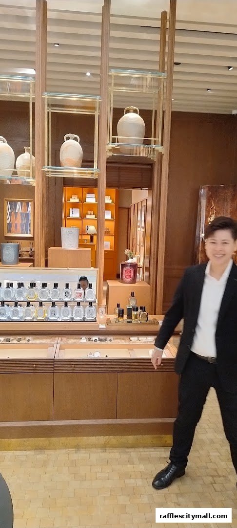 A person in a suit stands in a Diptyque store with perfume bottles and decorative vases on display.