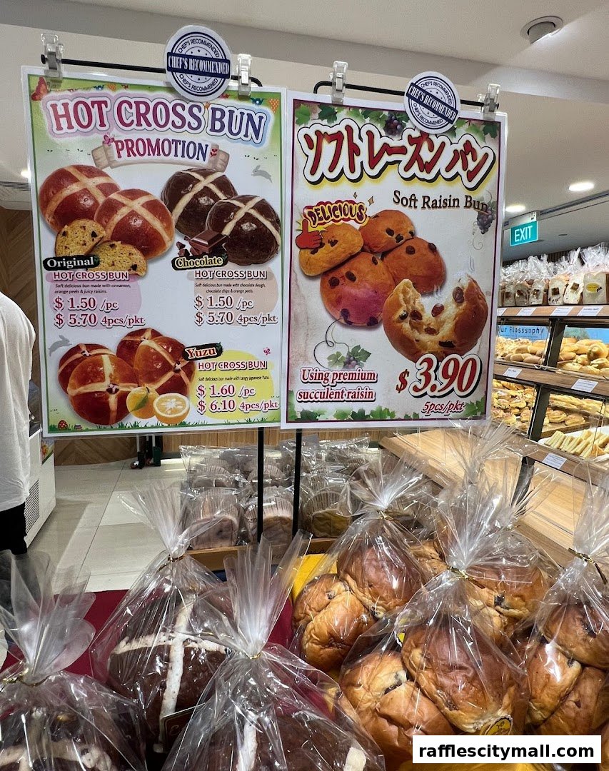 A display of freshly baked hot cross buns and raisin buns with promotional pricing.